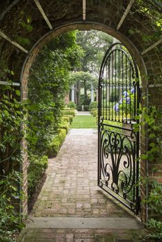 an iron gate in the middle of a brick walkway surrounded by greenery and trees