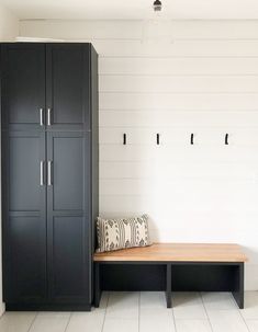 a bench and cabinets in a room with white tile flooring on the walls, along with two black lockers