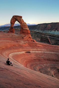 a person sitting on top of a large rock formation in the middle of desert land