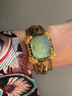 "This exquisite  archeological-revival bangle is attributed to Robert Phillips, circa 1865. The hinged bangle is decorated with Egyptian hieroglyphs in glossy black enamel culminating in a jade intaglio with a covered compartment to the reverse. \"ذات تو مظهر انعام سبحانی باد\", written in Farsi, it translates to, \"May your essence be a manifestation of divine blessings.\" A beautiful sentiment of well-wishing and hope for a positive and spiritually enriched existence. Hand fabricated in 15 karat gold, this bangle fits a petite 6\" wrist. A rare and wonderful jewel.    Weight: 28.1 grams Markings: none  Measurements: 6\" interior circumference, 1\" widest point (face) Notes: some losses to the enamel as shown" Traditional Jewelry With Historical Design For Collectors, Intaglio Bangle Bracelets As A Gift, Intaglio Bangle Bracelet As Gift, Intaglio Bangle Jewelry As A Gift, Antique Intaglio Ceremonial Jewelry, Antique Intaglio Jewelry For Ceremonial Occasions, Antique Ceremonial Intaglio Jewelry, Ceremonial Antique Yellow Gold Cuff Bracelet, Antique Carved Bangle Jewelry