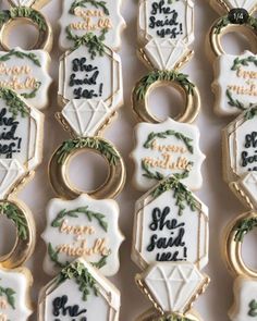 decorated cookies are arranged in rows on a white tablecloth with gold rings and greenery