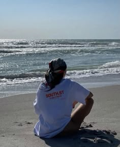 a woman sitting on the beach looking out at the ocean