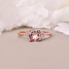 an oval morganite and diamond ring sits on a white flowered surface with petals in the background