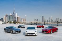 four different colored sports cars in front of a city skyline