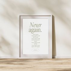 a white framed poster with the words never again in green on it next to a wooden table