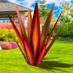 a large red plant in the middle of a yard with green grass and flowers behind it