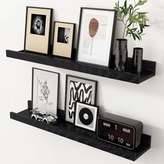 two black shelves with pictures and framed photographs on them, one shelf has an alarm clock