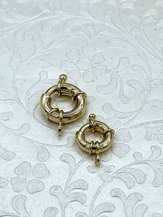 two pairs of gold toned hoop earrings on a white background with intricate designs in the background