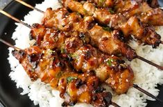 chicken skewers are served over rice on a black plate with chopsticks