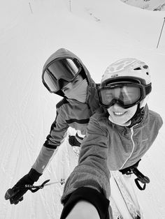 two people riding skis on top of a snow covered slope with goggles on