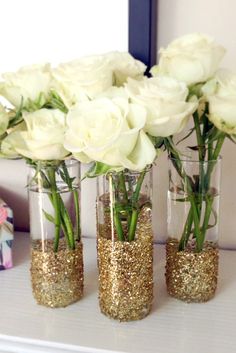 three clear vases with white roses in them on a shelf next to a mirror