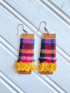 two pairs of colorful plaid fabric earrings hanging from wooden hooks on white wood planks