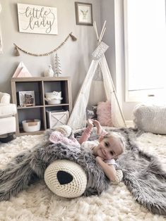 a baby laying on top of a furry rug next to a stuffed animal and teepee tent