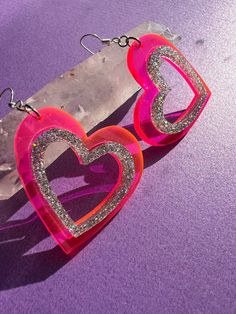 > hot pink and glitter acrylic heart shaped earrings are perfect for valentine's day or your next y2k look > a gift that sparkles * they would make a wonderful gift for someone who likes unique handmade jewelry * > the cut out hearts are laser engraved 1/8th inch thick acrylic with sterling silver ear wires > they are hypo-allergenic and nickel free  > the acrylic hearts are 1.75 inches wide and 1.72 inches long with a drop length of .5 inches  > feel free to message me if you would like to request a custom size > check my other listings for many other color options such as purple and iridescent  > find me on instagram @queen.beams for a firsthand look at how my items are made <3 Pink Heart Charm Earrings For Valentine's Day, Pink Heart Cut Earrings With Heart Charm, Pink Glitter Earrings For Valentine's Day, Pink Glitter Heart Earrings For Party, Trendy Pink Double Heart Earrings, Valentine's Day Pink Glitter Earrings, Valentine's Day Party Heart Earrings With Open Heart Shape, Pink Glitter Jewelry For Valentine's Day, Valentine's Day Pink Glitter Jewelry