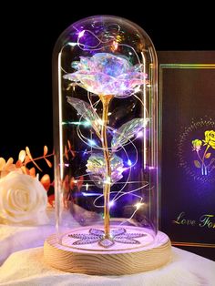 a lighted rose in a glass dome with flowers on the base and a card behind it