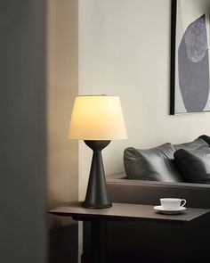 a table with a lamp on it next to a couch and coffee cup in the foreground