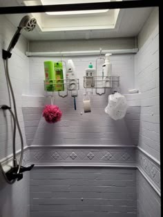 a bathroom with white brick walls and tiled flooring, shower head, toilet paper dispenser, and pink flowers in the corner