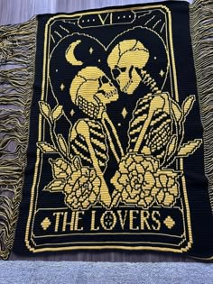 a black and yellow tapestry with two skeletons holding hands in the shape of a heart