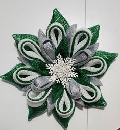 Add a touch of magic to your home with this stunning 20" Snowflake Flower Wreath. Crafted with vibrant emerald green foil mesh, this wreath features eye-catching accents of shimmering silver and crisp white foil mesh, creating a sparkling, frosty effect. At the heart of the wreath, a beautifully detailed white snowflake center completes the design, bringing an extra layer of elegance.   Perfect for the holiday season and beyond, this snowflake wreath will brighten your door or any interior space with its radiant glittering presence.  Whether hanging on your door or displayed in your living room, this wreath will make a statement and spread the spirit of the season throughout the winter months. Mesh Tube Wreath Diy, Hoco Braids, Birthday Wreath Diy, Christmas Snowflakes Wreath, Pancake Wreath, Foam Christmas Ornaments, Memorial Wreath, Christmas Wreath Designs, Decorative Mesh Wreaths