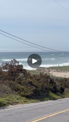 an empty road near the ocean with power lines above it