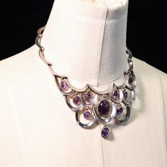 "Gorgeous necklace with a curved design and 10 cabochon set amethyst stones. Handcrafted, hinged, with abox closure on the back accented with an amethyst stone. The drops move very gently with the curved frame of the necklace. It is a beautiful piece. dated 1953-1979; Taxco, Mexico Antonio Pineda was a master silversmith who apprenticed with William Spratling. The maestro's work evolved from an early post-Mexican Revolutionary style influenced by a variety of themes that surrounded him, includin Silver Amethyst Necklace With Cabochon, Antique Handmade Amethyst Necklace, Luxury Amethyst Cabochon Necklace, Collectible Amethyst Necklace In Purple, Taxco Silver Jewelry Vintage, Colombian Art, Amethyst Stones, Bib Necklaces, Amethyst Stone