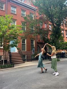 two women are dancing in the middle of an empty street with brick buildings behind them