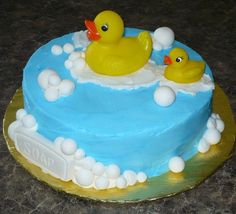 a blue cake with two rubber ducks in the bathtub on top and bubbles around it