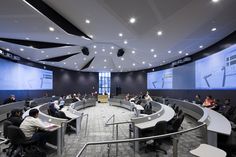 people are sitting at desks in an office setting with large screens on the walls