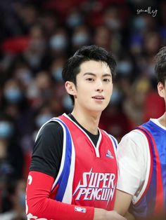 two young men standing next to each other in front of a basketball court with fans