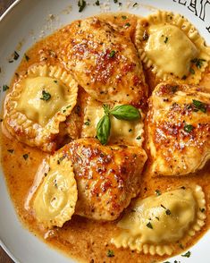 a white plate topped with ravioli covered in sauce and garnished with green leaves