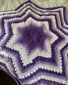 a purple and white crocheted blanket sitting on top of a bed