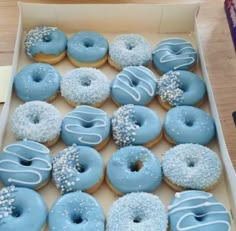 a box filled with blue frosted donuts covered in sprinkles on top of a wooden table