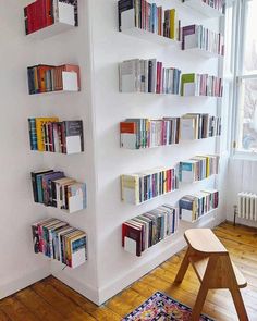 a white book shelf filled with lots of books next to a wooden chair and window