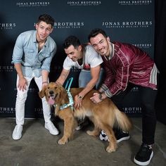 three men are posing for a photo with a dog on a leash in front of a black backdrop