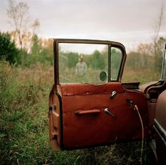 an old rusted car sitting in the middle of a field with its door open