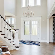 a large foyer with chandelier and two doors leading to another room that has a blue rug on the floor