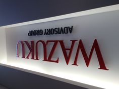 the wazuku advisory group sign is lit up in red and black letters on a white wall