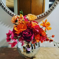 a vase filled with flowers sitting on top of a wooden table next to a mirror