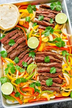 a tray filled with steak and vegetables on top of a table next to a tortilla