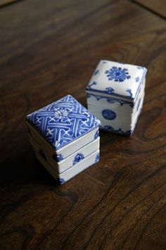 two small blue and white boxes sitting on top of a wooden table next to each other