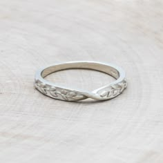 a silver ring sitting on top of a piece of wood with an intricate design in the middle