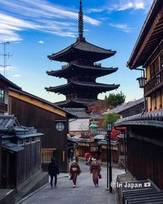 two people walking down a street in front of a tall building with a pagoda on top