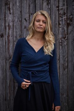 a woman standing in front of a wooden fence wearing a blue sweater and black skirt