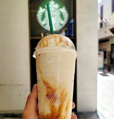 a hand holding up a starbucks drink in front of a building with a green straw