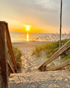 the sun is setting over the beach with stairs leading to the water's edge