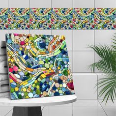 a mosaic tile wall hanging on the side of a bathtub next to a potted plant