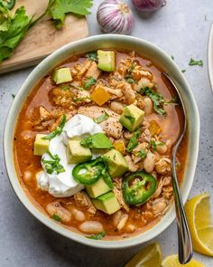 a bowl of chicken chili with sour cream, avocado and cilantro