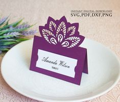 a purple and white place card sitting on top of a plate next to a plant