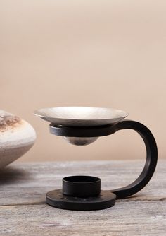 a white bowl sitting on top of a wooden table next to a black stand with a cup in it