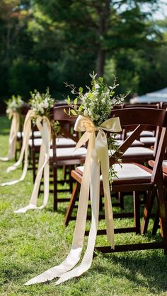 rows of wooden chairs with ribbons tied around them and flowers in vases on the back